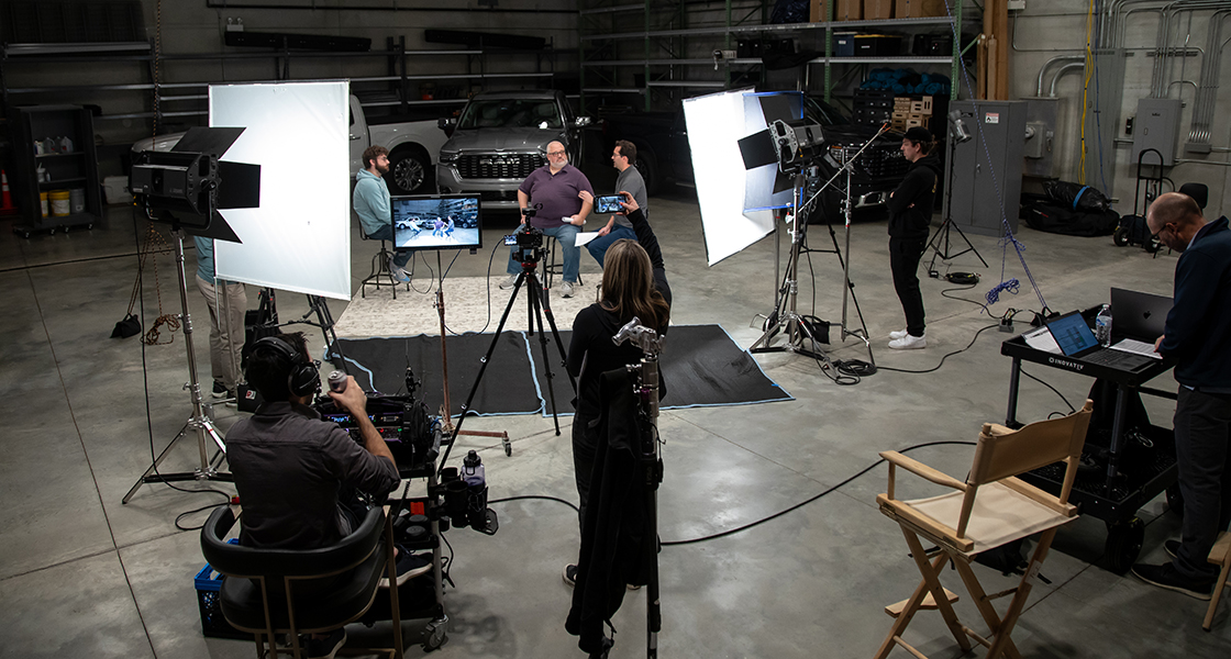 Production crew filming a video of three people talking in front of two trucks.