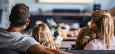 Back view of a relaxed family watching TV on sofa in the living room.