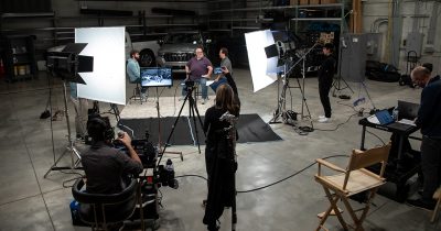 Production crew filming a video of three people talking in front of two trucks.