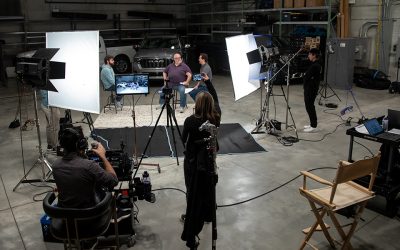 Production crew filming a video of three people talking in front of two trucks.