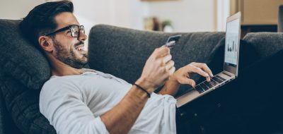 Smiling man lying on the couch and shopping online with credit card and laptop